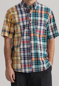 Camisa de cuadros de manga corta en varios colores: amarillo, azul marino, teal y rojo, con cuello abotonado y bolsillo en el pecho. Diseño de patrones mezclados.