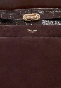 Brown suede handbag with a glossy, patterned dark brown leather flap. Features a gold clasp and the embossed logo "Dune LONDON."