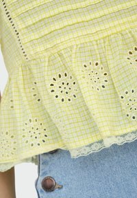 Yellow gingham top with lace trim and embroidered details; tiered ruffle hem; paired with light blue denim shorts featuring button accents.