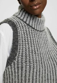 Gilet a collo alto in maglia grigia e grigia chiara con un motivo texture, caratterizzato da un colletto alto e ampie aperture per le braccia, che mostra i dettagli del tessuto morbido.