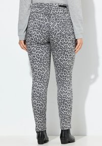 Leggings con stampa leopardata in grigio e nero, caratterizzati da un design aderente, vita media e tasche posteriori. Il materiale sembra liscio con una leggera elasticità.