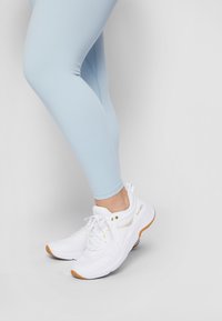 Ljusblå träningsleggings med en slät textur, tillsammans med vita sneakers med guldaccenter och gummisula.