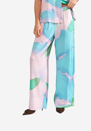 Široké nohavice s pastelovým abstraktným vzorom v modrej, ružovej a zelenej farbe, doplnené zodpovedajúcou košeľou a hnedými špicatými topánkami.