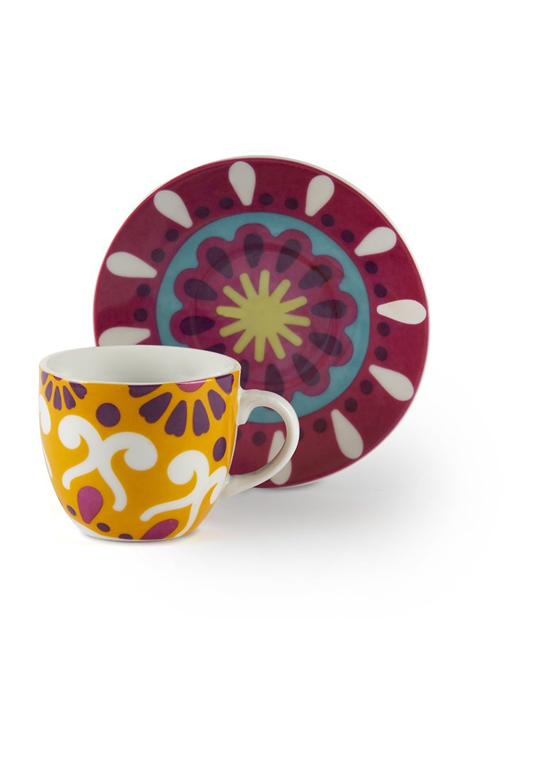 Kopp med vit handtag och gula, vita och lila blommönster framför en rund underkop med röd, blå, gul och vit dekorativ design.