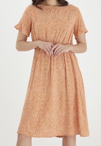 Krótkosleeve sukienka w kształcie litery A w pomarańczowym kolorze z białym abstrakcyjnym wzorem, z elastycznym pasem i miękkim, lekkim materiałem.