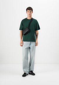 Zelené bavlněné tričko, volný střih, v kombinaci s světle modrými džíny. Černá crossbody taška se strapcem a černé tenisky.