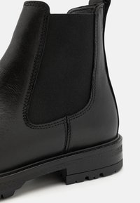Black leather Chelsea boot featuring a textured elastic side panel, rugged sole, and reinforced stitching details along the seams.