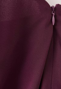 Gros plan sur un tissu de vêtement violet foncé avec une fermeture éclair visible sur le côté droit.