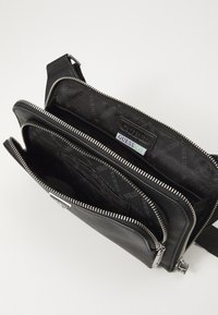Borsa a tracolla in pelle nera con hardware argentato, dotata di più scomparti con zip e di una fodera interna con marchio caratterizzata da motivi ripetuti.