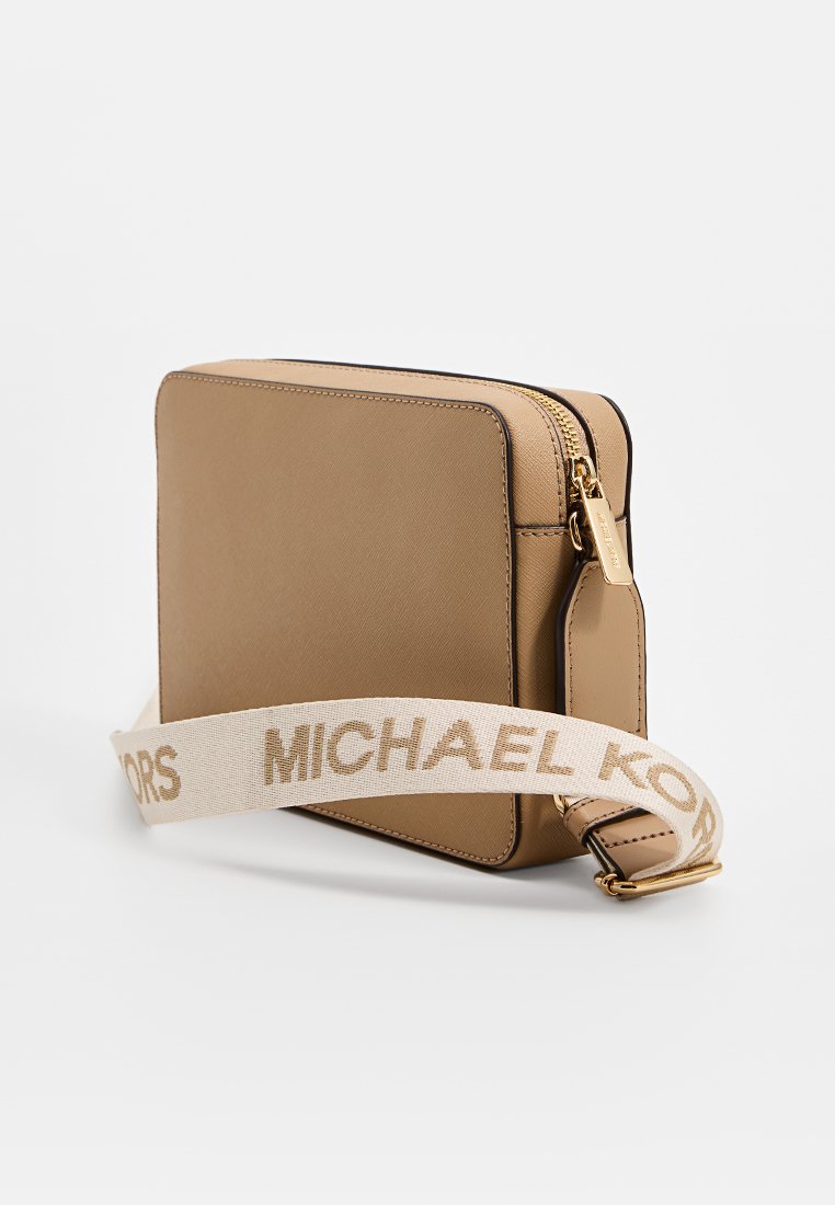Sac en cuir tan rectangulaire à bandoulière avec fermeture éclair dorée et sangle en tissu beige réglable imprimée avec "MICHAEL KORS" en lettres majuscules.