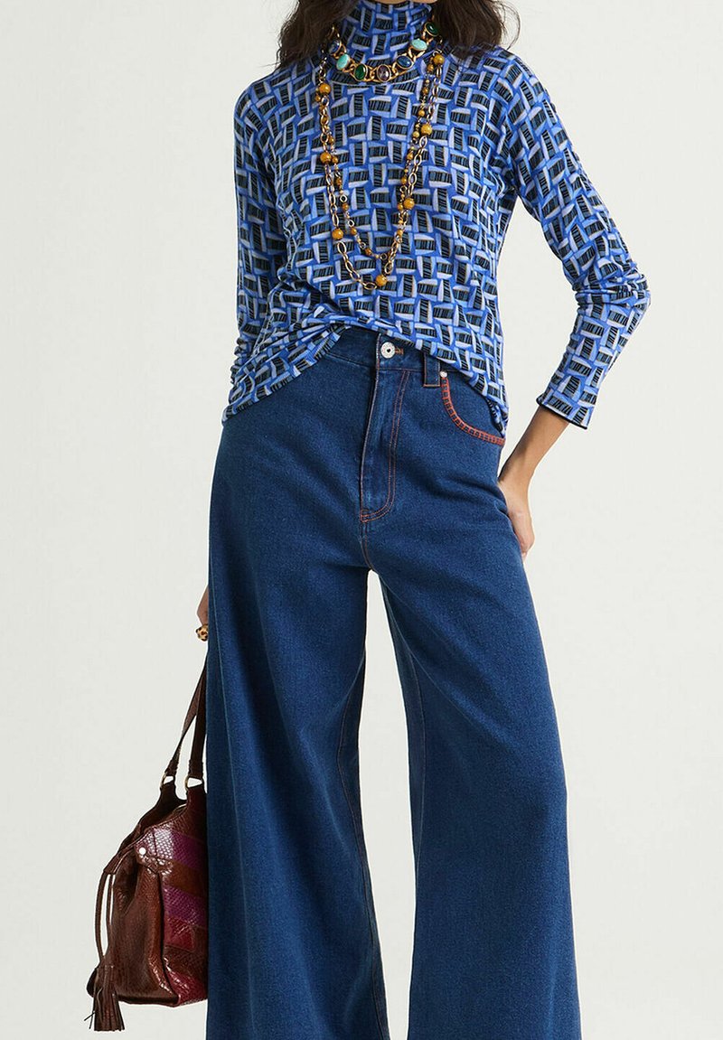 Maglia a maniche lunghe con collo alto e motivo blu abbinata a jeans scuri in denim a gamba larga e vita alta. Accessoriata con collane a strati e una borsa.