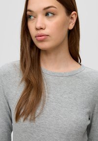 Grauer Langarmshirt mit gerippter Textur und rundem Ausschnitt, getragen von einer Person mit langen braunen Haaren, die die Weichheit des Stoffes zur Schau stellt.