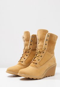 Bottes compensées en daim camel avec doublure en fourrure, lacets à l'avant et semelles en caoutchouc conçues pour les temps froids.