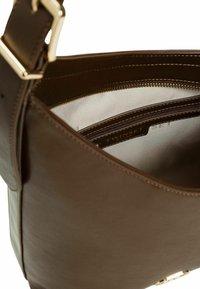 Borsa in pelle marrone con una texture liscia, dotata di una fibbia in metallo di colore oro. L'interno presenta diversi scomparti con una fodera a righe chiare.