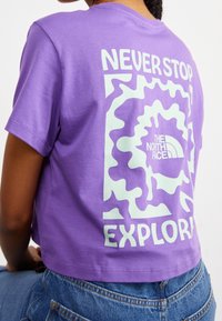 Purple cotton t-shirt with short sleeves, featuring a mint green graphic design and text on the back that reads "NEVER STOP EXPLORING."