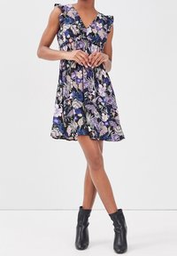 Robe florale avec un fond noir ornée de motifs floraux roses et violets, des manches à volants et une jupe évasée. Portée avec des bottines noires.