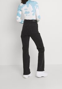 Svarta högmidjade jeans med rak bendesign, tillverkade av denim, visade tillsammans med en vit och blå mönstrad topp och chunky vita skor.