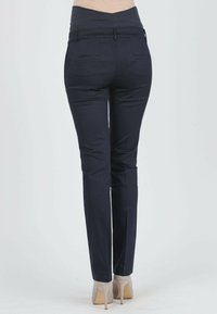 Dunkelblaues Hosenpaar mit einer taillierten Passform, dehnbarem Bund und zwei Gesäßtaschen. Tragen mit hellen High Heels. Glatte Textur.