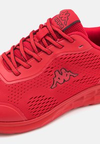Scarpa sportiva rossa con tomaia in rete per la traspirabilità, suola in gomma solida e dettaglio del logo nero sul lato. I lacci sono centrali e testurizzati.