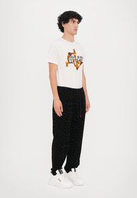 Bela majica s kratkimi rokavi z barvitim logotipom "Versace Jeans Couture", kombinirana z črnimi športnimi hlačami z vzorcem in belimi chunky supergami.