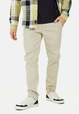 Beige cotton pants with a slim fit, worn with a black t-shirt and a plaid button-up shirt featuring green and yellow accents. White sneakers.