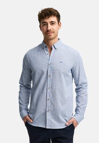 Camisa de cuadros azul claro con mangas largas, fabricada en tejido entrelazado. Presenta botones marrones y un pequeño logotipo bordado.