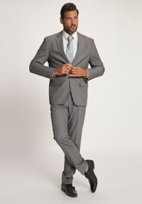 Completo grigio con giacca su misura e pantaloni aderenti, arricchito da una cravatta a motivi blu chiaro e scarpe in pelle nera, su uno sfondo neutro.