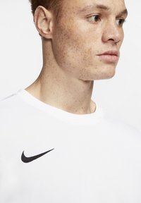 Witte T-shirt met korte mouwen van zachte stof, met een zwart Nike-logo op de linkerborst, een ronde halslijn en een gladde textuur.