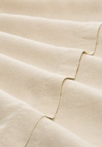 Tessuto di lino beige chiaro con una texture liscia, caratterizzato da pieghe ordinate e dettagli di cucitura sottili.
