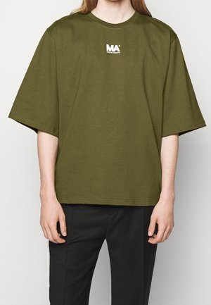 T-shirt oversize verde oliva in cotone, con scollatura rotonda e un piccolo logo bianco sul petto. Maniche corte, vestibilità comoda.