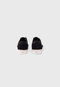 Čierne semišové slip-on topánky s bielou gumovou podrážkou, s prešívaným dizajnom a logom na päte. Hladký povrch, minimálne detaily.