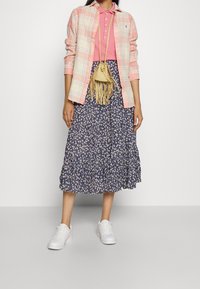 Camisa de cuadros rosa de manga larga, polo rosa, falda midi floral azul marino con volantes y zapatillas blancas. Pequeño bolso cruzado beige con flecos.