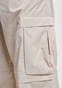Pantalons cargo beige en tissu léger, dotés d'une grande poche latérale, de détails de couture visibles et d'une coupe décontractée et ample.