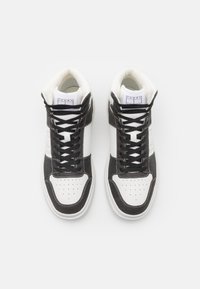 Vysoké tenisky s bílou koženou špičkou, černými látkovými stranami a černými tkaničkami. Na jazyku je logo na štítku a perforace zajišťují ventilaci.