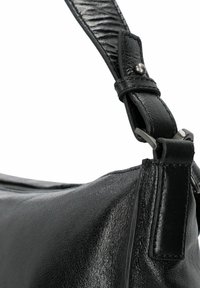 Detalle de un bolso de cuero negro con acabado texturizado, correa ajustable con herrajes metálicos y una forma elegante y curvada.