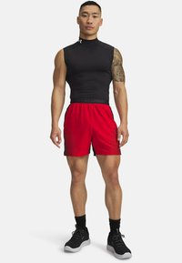 Top negro sin mangas con un escote alto, combinado con pantalones cortos rojos con acentos negros y una textura de malla, complementado con zapatillas deportivas negras.