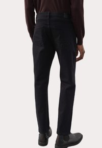 Jeans in denim nero con taglio dritto, dotati di due tasche posteriori e una vita visibile; abbinati a stivali alla caviglia in pelle marrone.