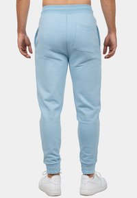 Lichtblauwe joggingsbroek van zachte stof, met een taps toelopende pijp, elastische tailleband en achterzak. Gepaard met witte sneakers.