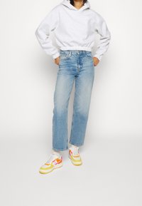 Grey hooded sweatshirt with elastic hem, blue straight-leg jeans, and white sneakers featuring yellow and pink accents.