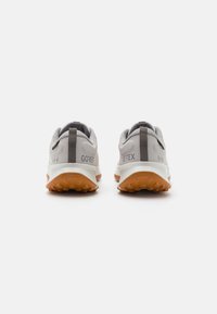 Las zapatillas de running GORE-TEX presentan una parte superior gris, suela texturizada en color naranja, cuello acolchado y una lengüeta para ponerlas y quitarlas fácilmente.