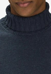 Mörk marinblå polotröja med ribbad textur och en figurnära krage. Tyget verkar mjukt och stickat, med ett subtilt mönster.