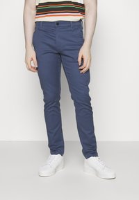 Niebieskie chinosy o dopasowanym kroju wykonane z bawełny. Posiadają zapięcie na guziki, szlufki na pasek oraz boczne kieszenie. Połączone z białymi trampkami.