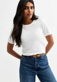 Camiseta blanca de manga corta hecha de tejido suave, combinada con unos vaqueros de mezclilla azul de tiro alto y un cinturón marrón con hebilla dorada.