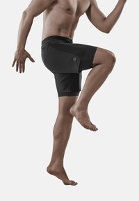 Zwarte sportshorts met een aansluitend ontwerp en zijzak, rekbare stof, gestructureerde tailleband en een lengte tot halverwege het bovenbeen. Model op blote voeten.