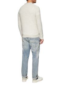 Pull en tricot blanc à col rond, associé à un jean en denim bleu clair légèrement déchiré et des baskets blanches.