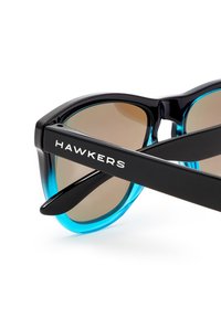 Ochelari de soare negri și albaștri cu lentile întunecate. Rama are un finisaj lucios și un design unghiular, cu marca "HAWKERS" pe braț.
