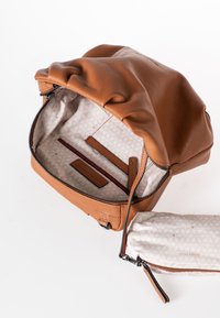 Bruine leren handtas met een opgevouwen bovenkant en ritssluiting. De gevoerde binnenkant heeft een geometrisch patroon, rode accenten en compartimenten voor organisatie.
