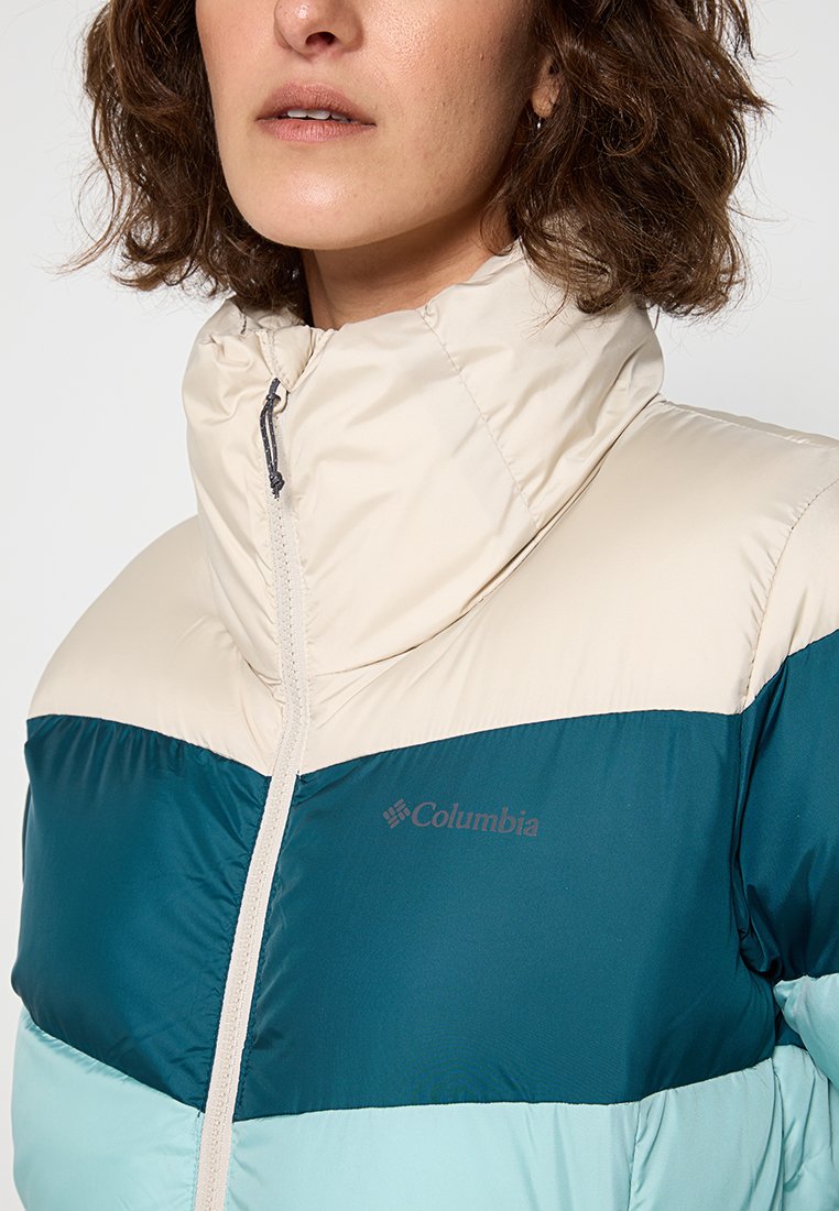 Chaqueta de plumas con bloques de color que presenta un diseño en crema, azul verdoso y azul claro, con cierre frontal, cuello alto y un logo en el pecho.