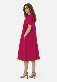 Fuchsia linnen jurk met korte mouwen, losse pasvorm, knie-length, met zijzakken en een ronde hals. Gecombineerd met beige sleehakken.