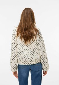 Gequilted jas met een crèmekleurige achtergrond en blauwe bloemenpatronen, elastische manchetten en een geplooide zoom. Draagt met blauwe jeans.